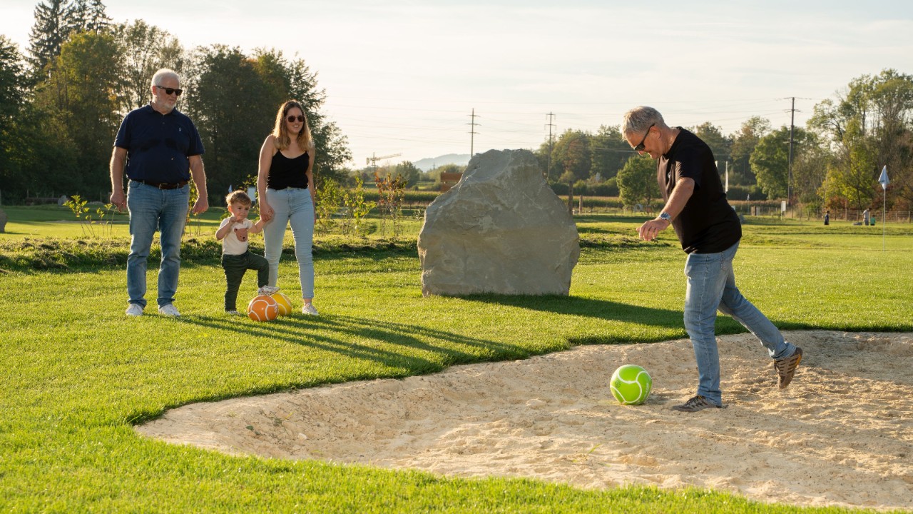 A family playing football golf on an area of grass and sand.